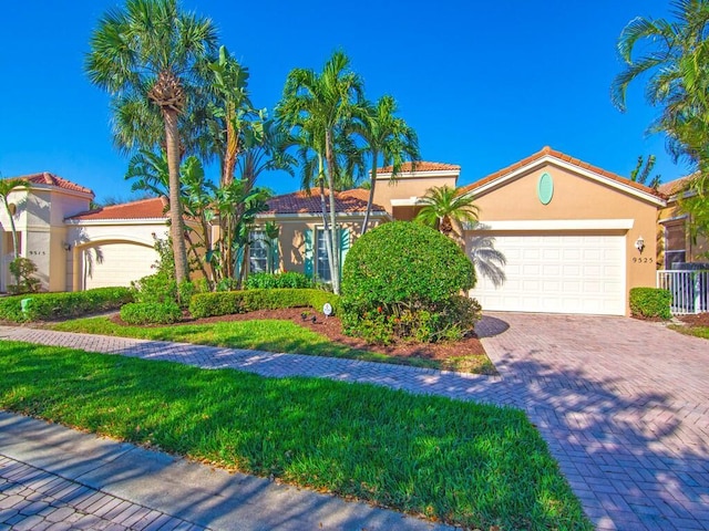 view of front of house featuring decorative driveway, stucco siding, a front yard, a garage, and a tiled roof