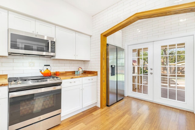 kitchen with white cabinets, wood counters, appliances with stainless steel finishes, light wood-style floors, and backsplash