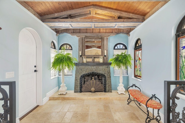 unfurnished living room featuring lofted ceiling with beams, stone tile floors, baseboards, wooden ceiling, and a stone fireplace