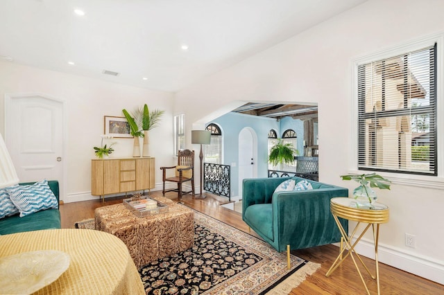 living area with arched walkways, wood finished floors, visible vents, and baseboards