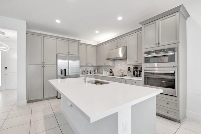 kitchen with backsplash, under cabinet range hood, gray cabinets, appliances with stainless steel finishes, and a sink