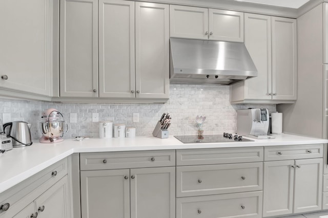 kitchen featuring under cabinet range hood, black electric cooktop, decorative backsplash, and light countertops