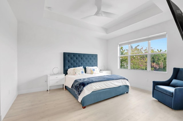 bedroom with a ceiling fan, a tray ceiling, light wood-style floors, and baseboards