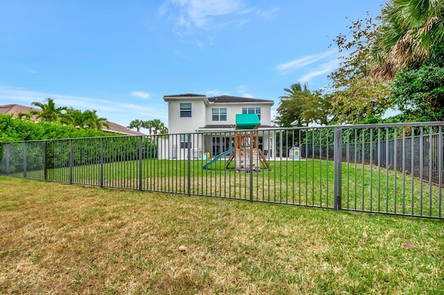 back of house with a fenced backyard, stucco siding, a playground, and a yard