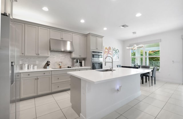 kitchen featuring visible vents, a sink, gray cabinetry, under cabinet range hood, and backsplash