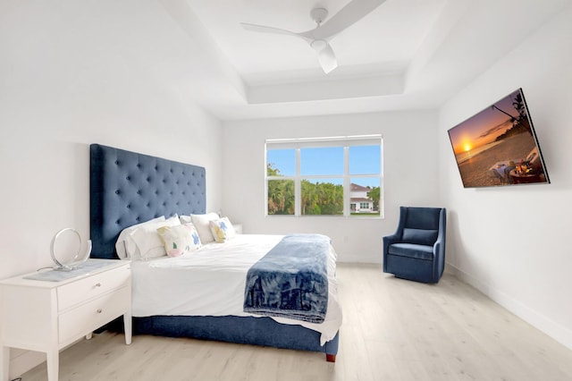 bedroom with a tray ceiling, wood finished floors, baseboards, and ceiling fan