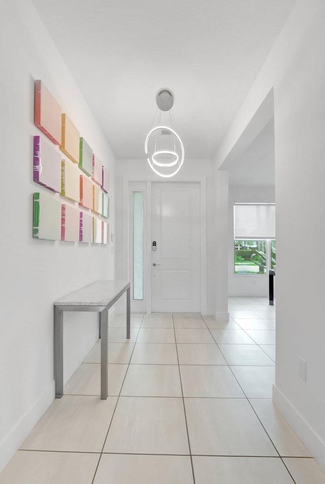 hallway featuring baseboards, a notable chandelier, and light tile patterned flooring