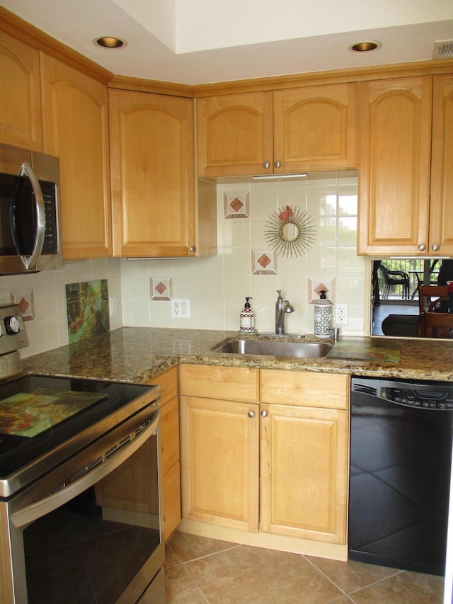 kitchen featuring stainless steel appliances, decorative backsplash, light brown cabinetry, a sink, and dark stone countertops