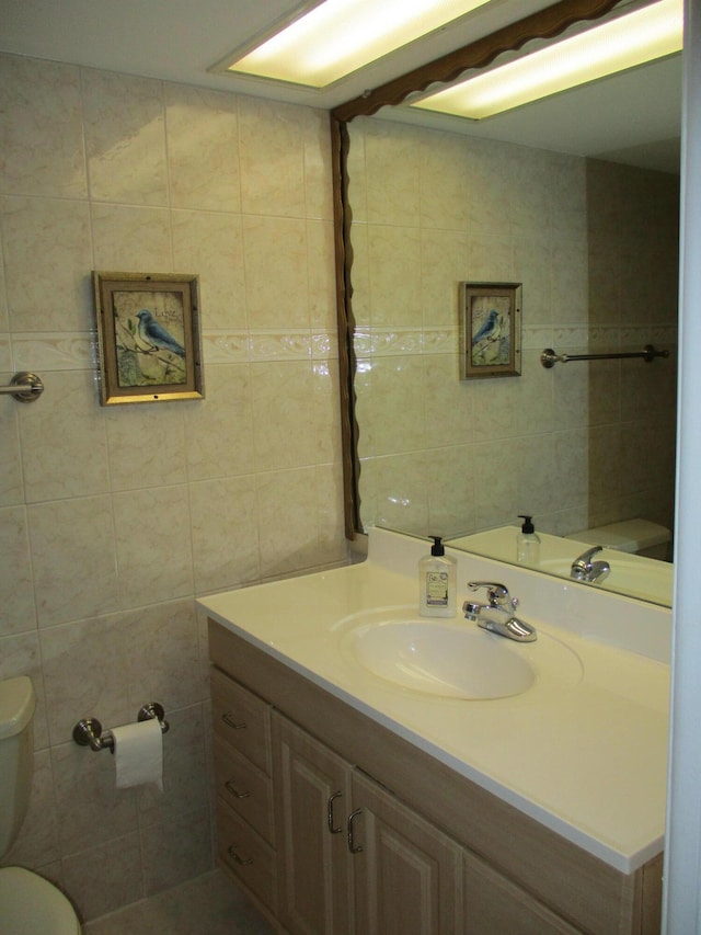 bathroom featuring toilet, vanity, and tile walls