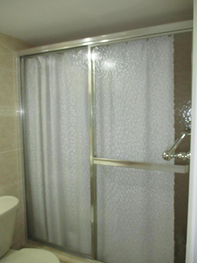 full bathroom featuring a shower with door and toilet