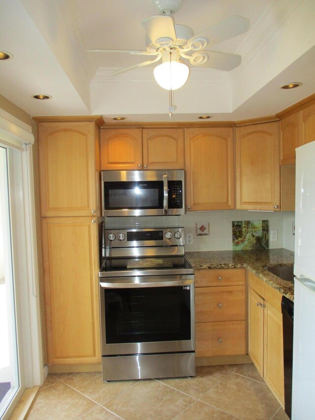 kitchen with light brown cabinets, stainless steel appliances, a tray ceiling, dark stone countertops, and crown molding