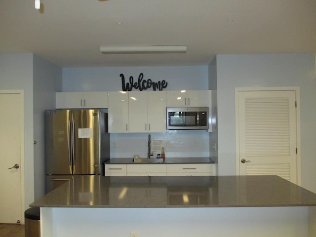 kitchen with tasteful backsplash, dark countertops, a kitchen island, stainless steel appliances, and white cabinetry