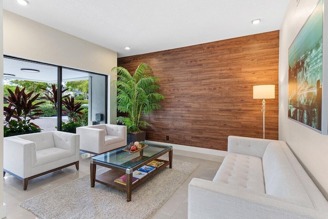 living area featuring wood walls, a textured ceiling, baseboards, and light tile patterned floors