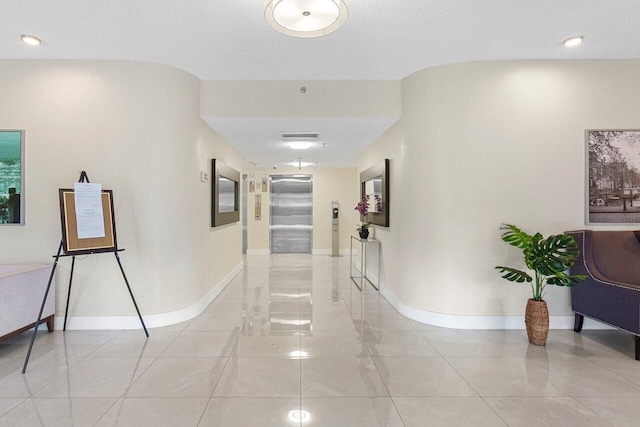 corridor with elevator, light tile patterned floors, baseboards, and a textured ceiling