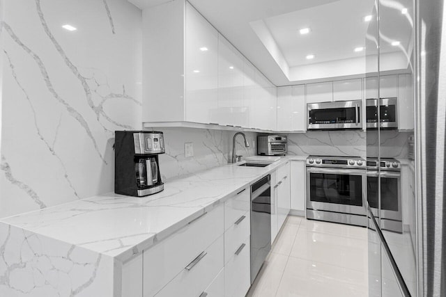 kitchen with light stone counters, stainless steel appliances, white cabinets, a sink, and modern cabinets