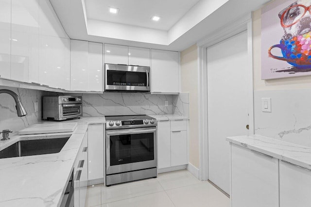 kitchen with white cabinets, modern cabinets, appliances with stainless steel finishes, a sink, and backsplash