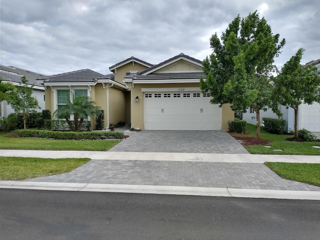 view of front of property with a front yard, decorative driveway, an attached garage, and stucco siding