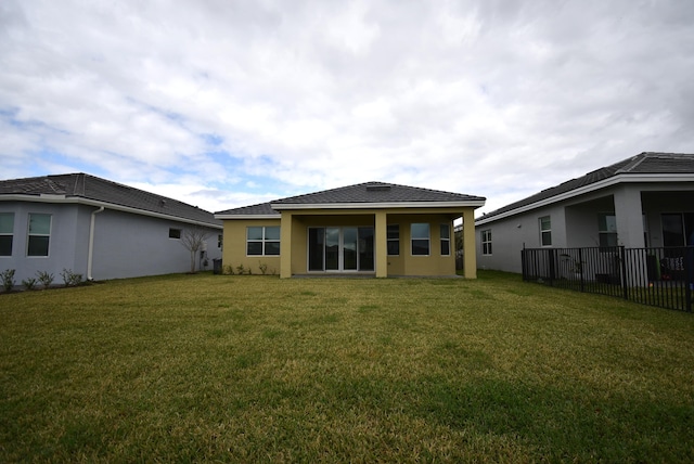 rear view of house featuring a yard, fence, and stucco siding