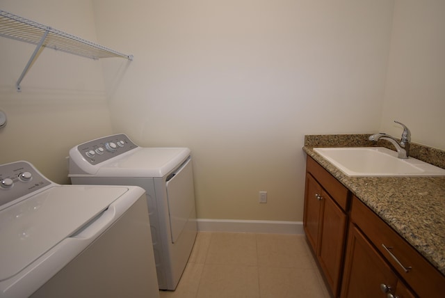 clothes washing area featuring light tile patterned flooring, laundry area, a sink, baseboards, and washing machine and clothes dryer