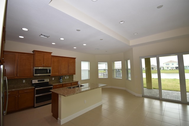 kitchen with stone counters, a water view, backsplash, appliances with stainless steel finishes, and a sink