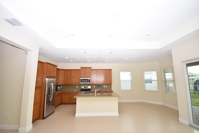 kitchen featuring a tray ceiling, brown cabinets, stainless steel appliances, visible vents, and backsplash