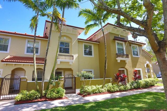 mediterranean / spanish home with a fenced front yard, a tile roof, a gate, and stucco siding