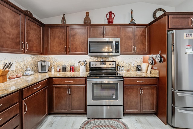 kitchen with backsplash, appliances with stainless steel finishes, vaulted ceiling, and light stone counters