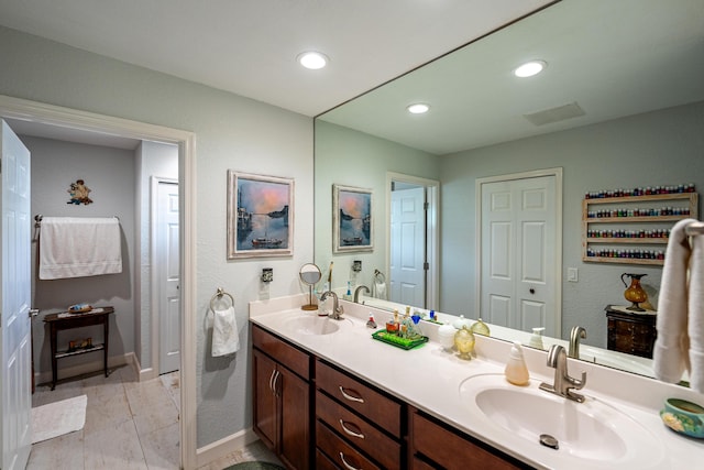 bathroom featuring double vanity, baseboards, a sink, and recessed lighting