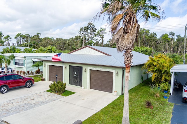 ranch-style house with metal roof, an attached garage, driveway, stucco siding, and a front yard