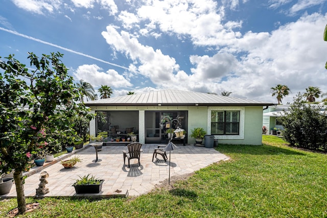 rear view of house with stucco siding, metal roof, a lawn, and a patio