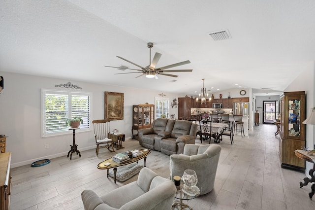 living room featuring lofted ceiling, ceiling fan with notable chandelier, visible vents, baseboards, and light wood-style floors