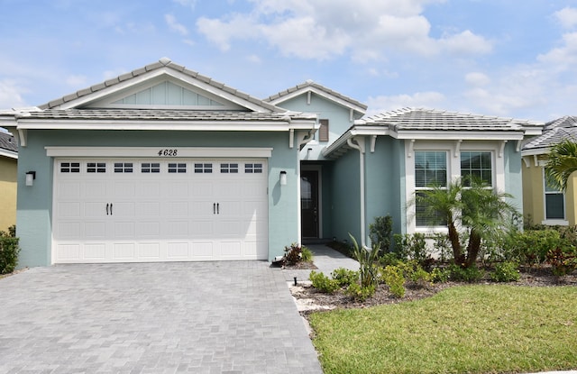 single story home featuring a garage, decorative driveway, a tile roof, and stucco siding