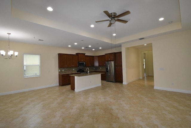 kitchen featuring appliances with stainless steel finishes, a tray ceiling, open floor plan, and a center island with sink