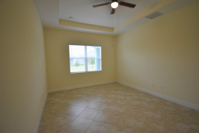 unfurnished room featuring a tray ceiling, visible vents, light tile patterned flooring, ceiling fan, and baseboards