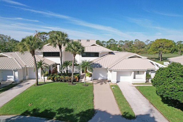 view of front of home featuring metal roof, concrete driveway, a front yard, and a standing seam roof