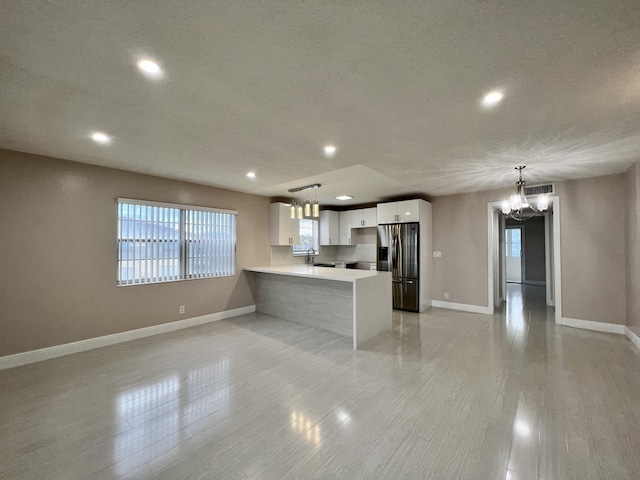 kitchen featuring white cabinets, a notable chandelier, light countertops, stainless steel refrigerator with ice dispenser, and a sink