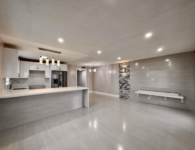 kitchen with light countertops, white cabinetry, a sink, a peninsula, and stainless steel fridge with ice dispenser