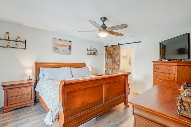 bedroom with ceiling fan, ensuite bathroom, light wood-style floors, and a barn door