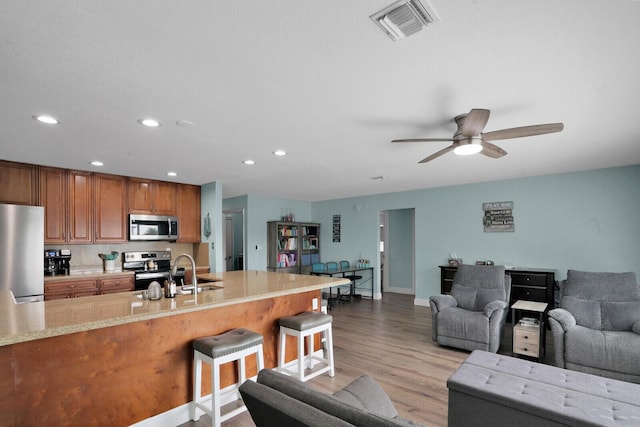 kitchen featuring light wood finished floors, visible vents, a breakfast bar area, brown cabinetry, and stainless steel appliances