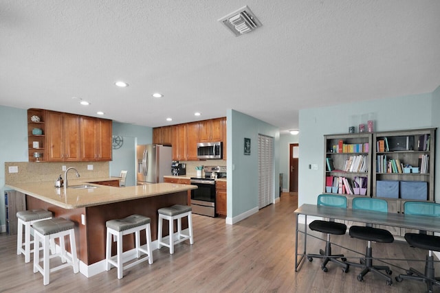 kitchen with visible vents, a peninsula, brown cabinetry, stainless steel appliances, and a sink