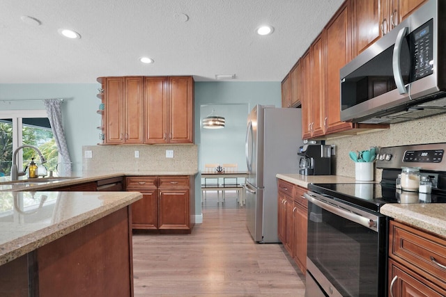 kitchen with brown cabinets, a sink, light stone counters, light wood-style floors, and appliances with stainless steel finishes