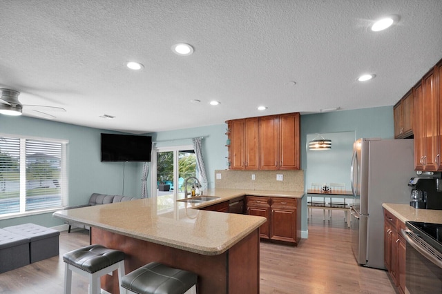 kitchen with light wood-type flooring, a sink, a kitchen breakfast bar, a peninsula, and decorative backsplash