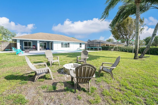 view of yard featuring a patio, a trampoline, fence, a fire pit, and an outdoor pool