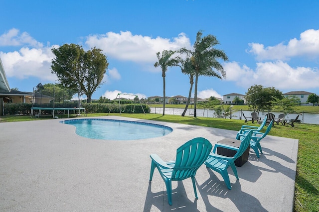 outdoor pool with a lawn, a patio, a trampoline, and a water view