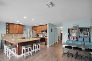 kitchen featuring brown cabinets, a breakfast bar area, visible vents, and stainless steel appliances