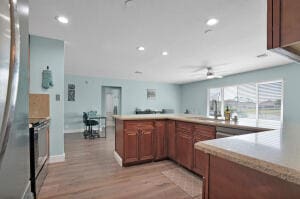 kitchen with a ceiling fan, light wood finished floors, range with electric cooktop, light countertops, and brown cabinets