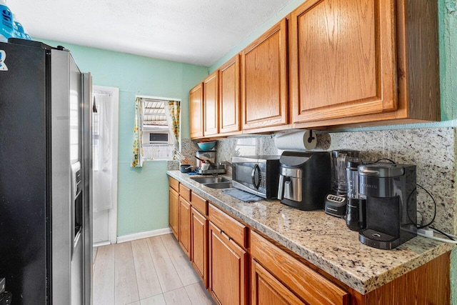 kitchen featuring light wood finished floors, appliances with stainless steel finishes, brown cabinetry, a sink, and baseboards