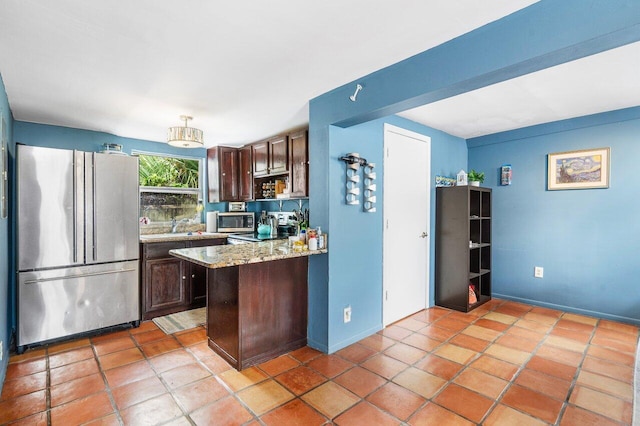 kitchen with light tile patterned floors, stainless steel appliances, light stone counters, and dark brown cabinetry