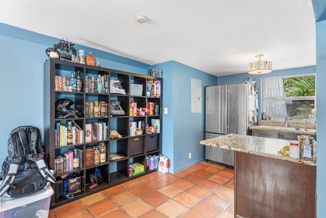 kitchen featuring tile patterned flooring, a sink, freestanding refrigerator, and baseboards