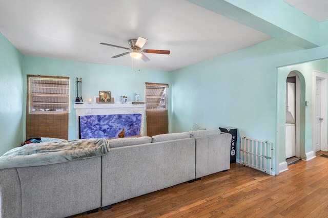 living area featuring arched walkways, wood finished floors, a ceiling fan, and baseboards